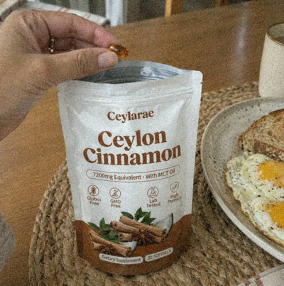 Hand holding one amber softgel above an open Ceylarae pouch at breakfast